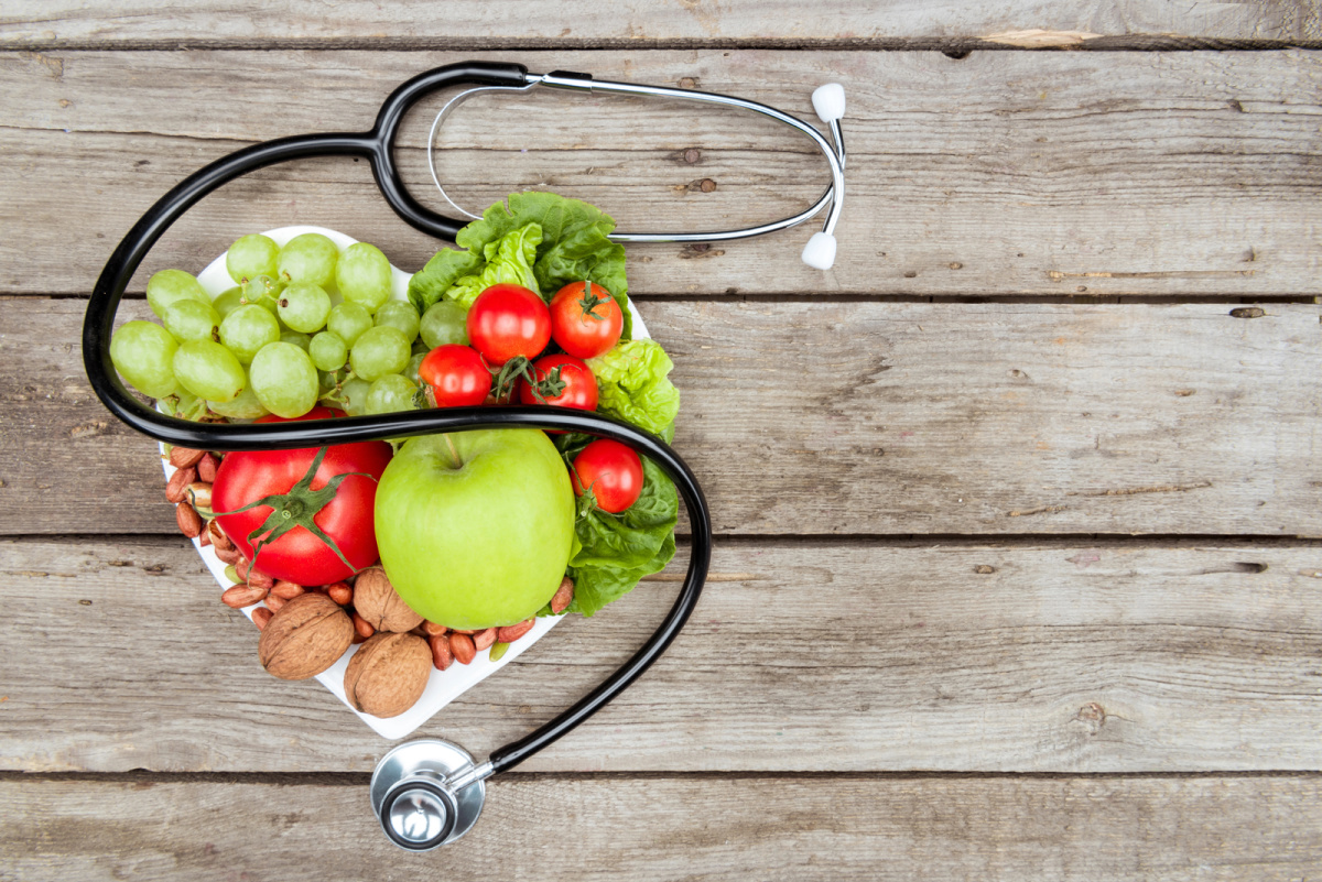 A heart shaped plate stacked with healthy foods and a stethoscope representing the need for a healthy diet after hiatal hernia surgery.