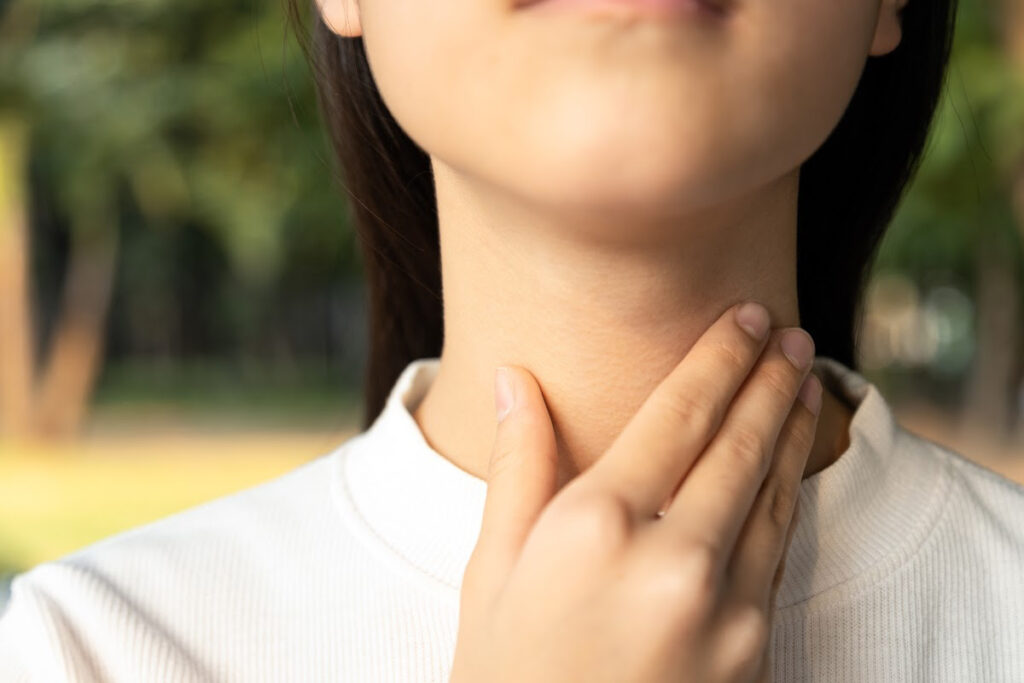 A woman holding her throat wondering if acid reflux can cause coughing.